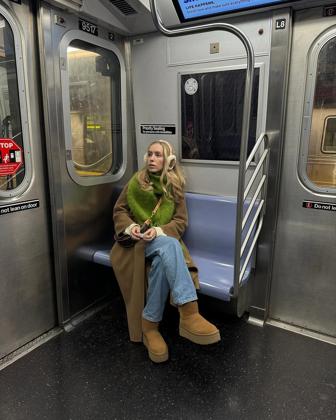 Person in brown coat, green scarf and jeans on subway