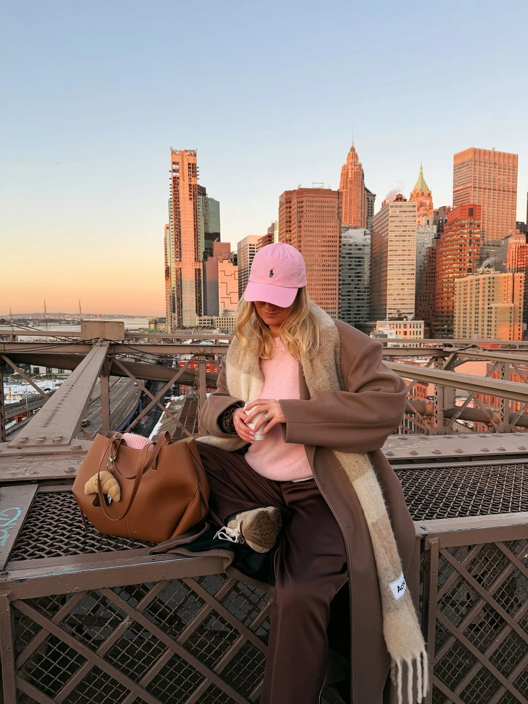 Person in taupe layers, pink cap and dark trousers on bridge