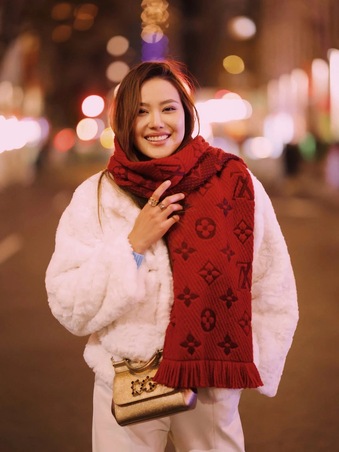 Person in cream shag-textured coat with red scarf at night