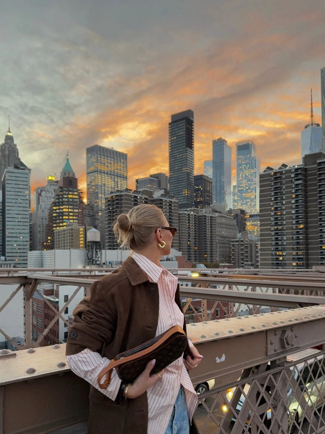 Person in brown jacket, striped shirt and light jeans on bridge