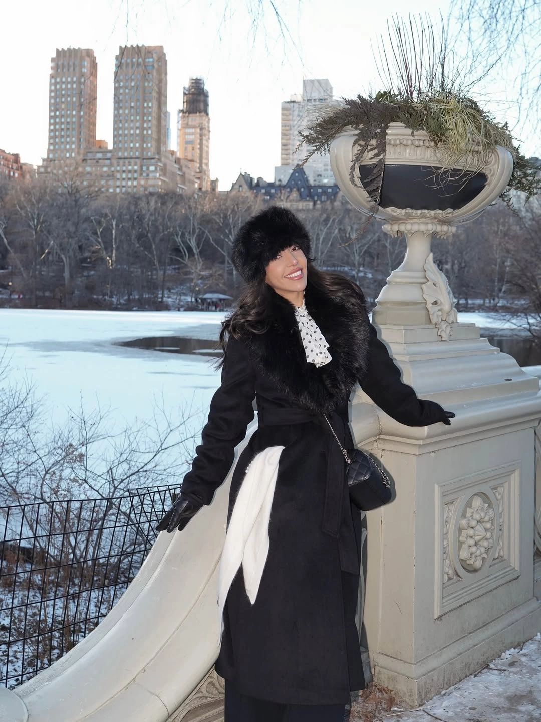 Person in black coat and fur-like hat near snowy railing