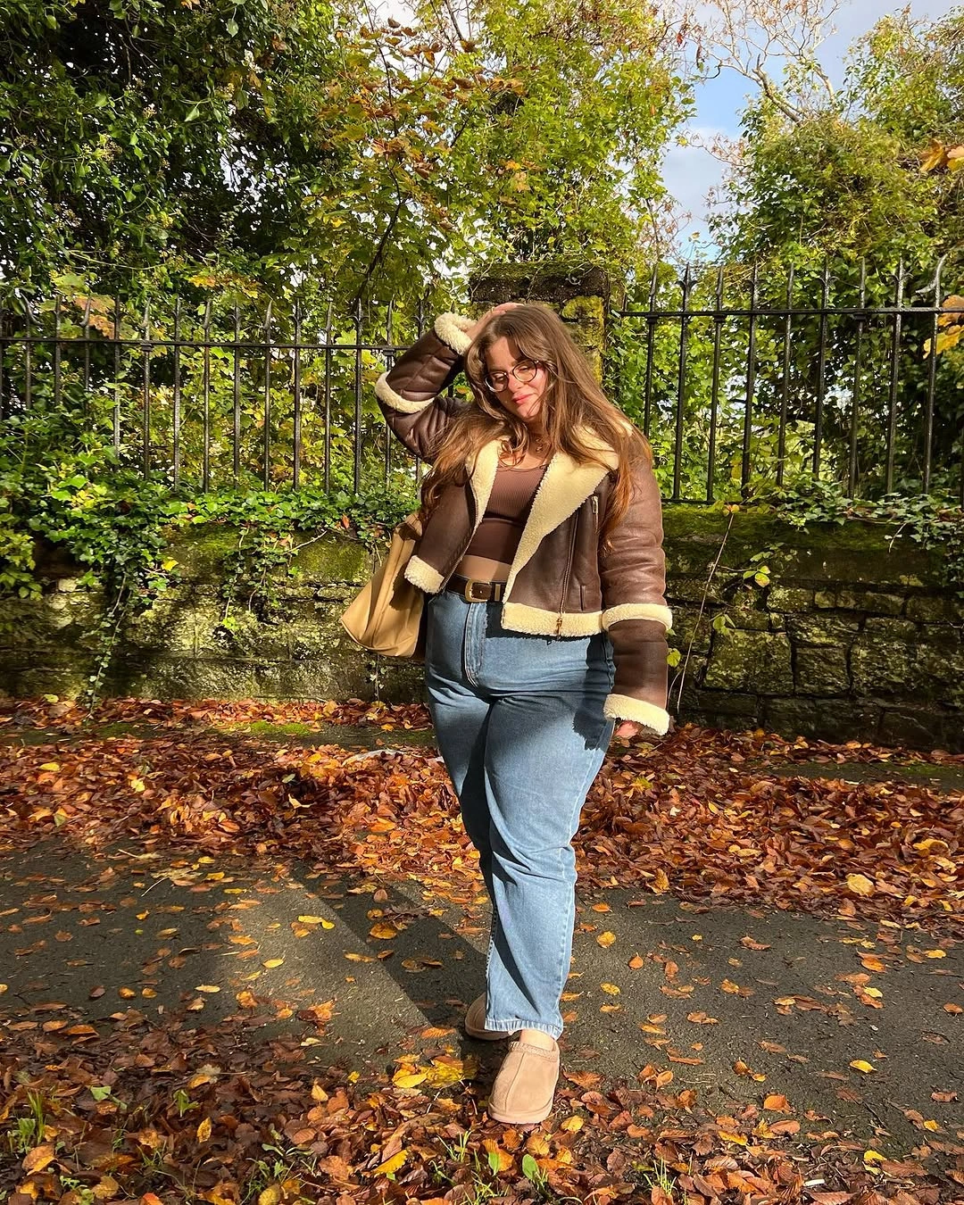 Brown trimmed jacket with blue jeans and tan shoes