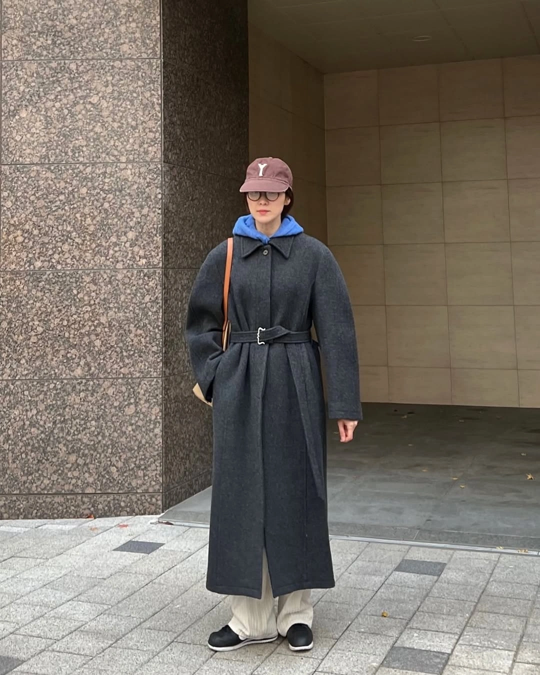 Gray belted coat with blue hoodie and pale trousers