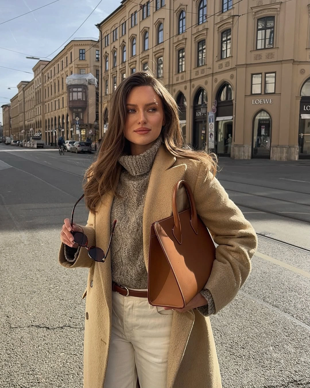 Camel coat with gray turtleneck, white trousers and brown bag