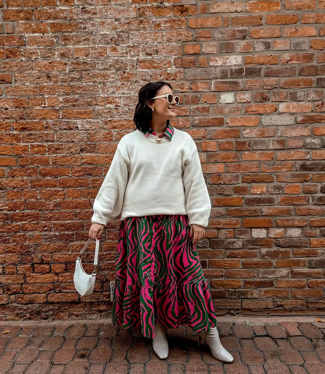 Cream sweatshirt with vivid patterned midi skirt, white ankle boots, and white bag