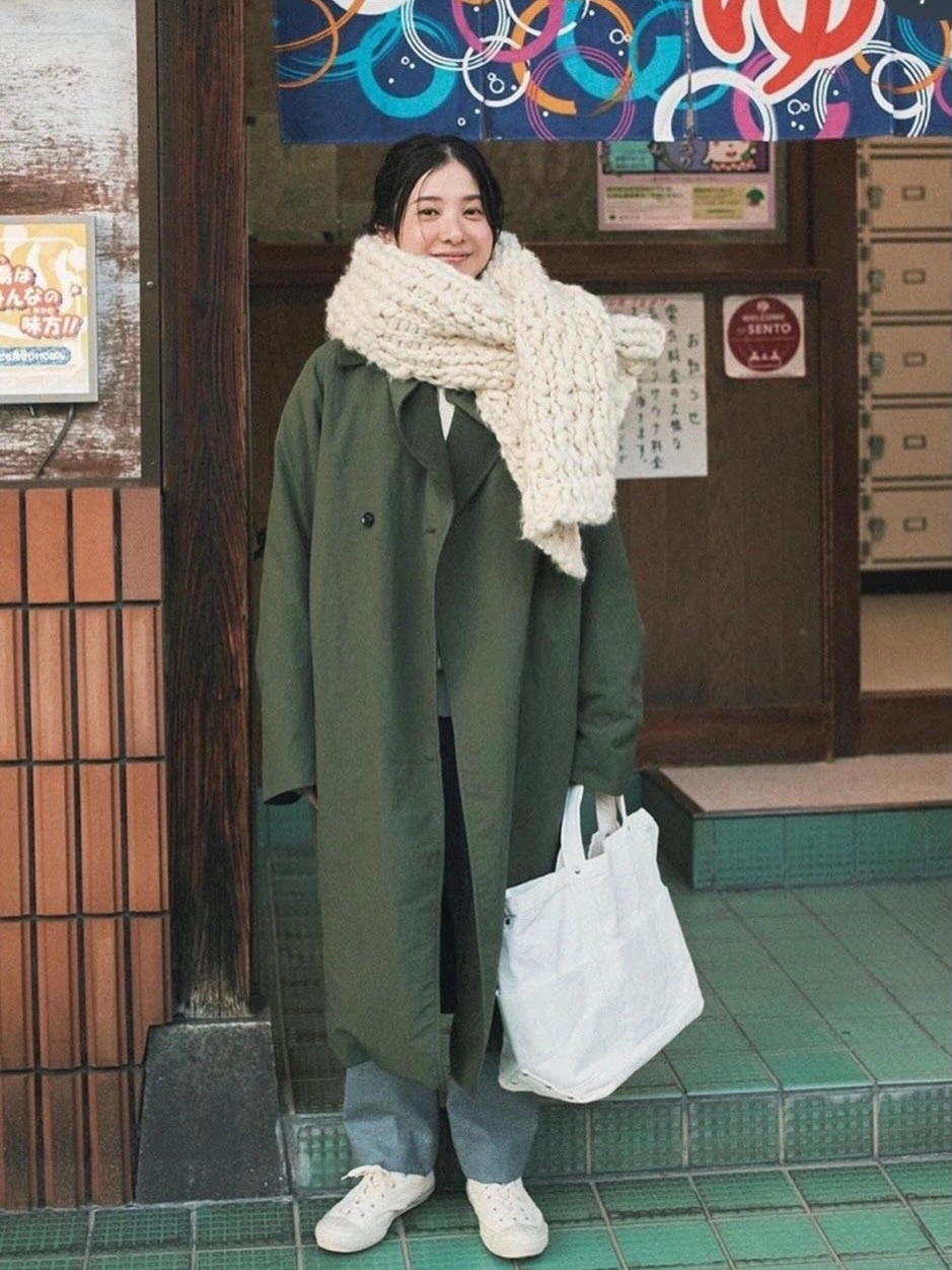 Long green coat with oversized cream scarf, loose jeans, white sneakers, and white tote