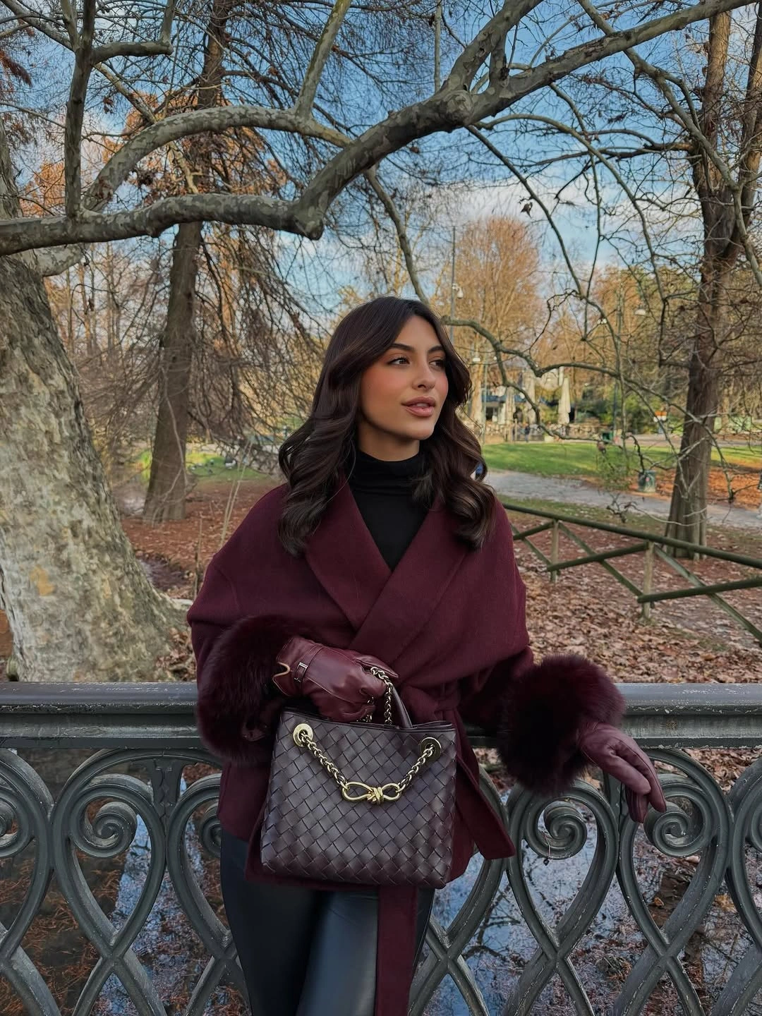 Burgundy wrap-style outer layer with large cuffs, dark turtleneck, and chain-detail bag