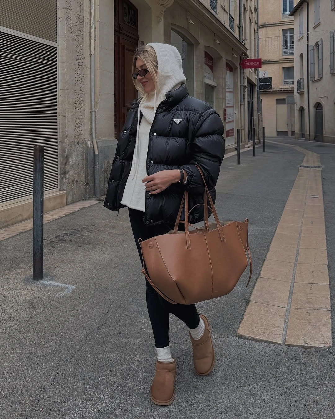 Black puffer jacket with white hood, black leggings, tan tote, and tan ankle boots