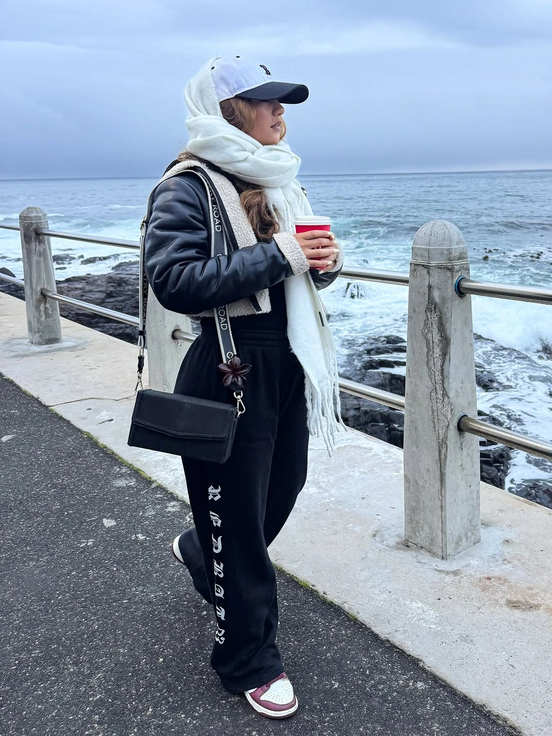 Black outer layer and joggers with white hoodie, wide scarf, red and white sneakers, and black bag