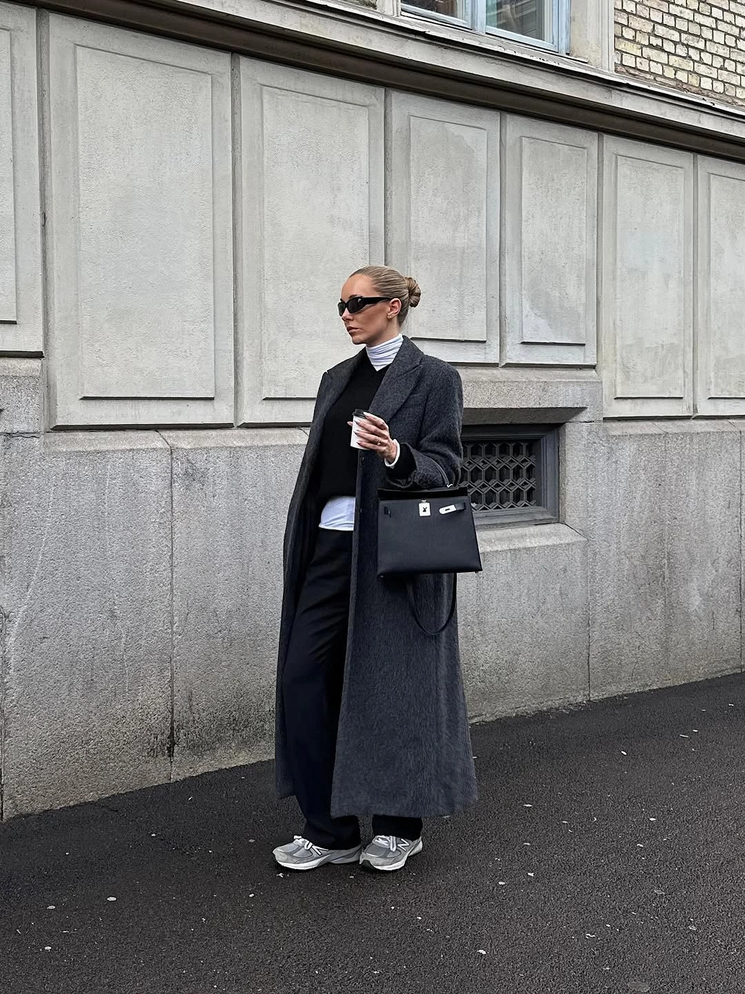 Long black coat with striped top, dark trousers, sneakers, and black bag
