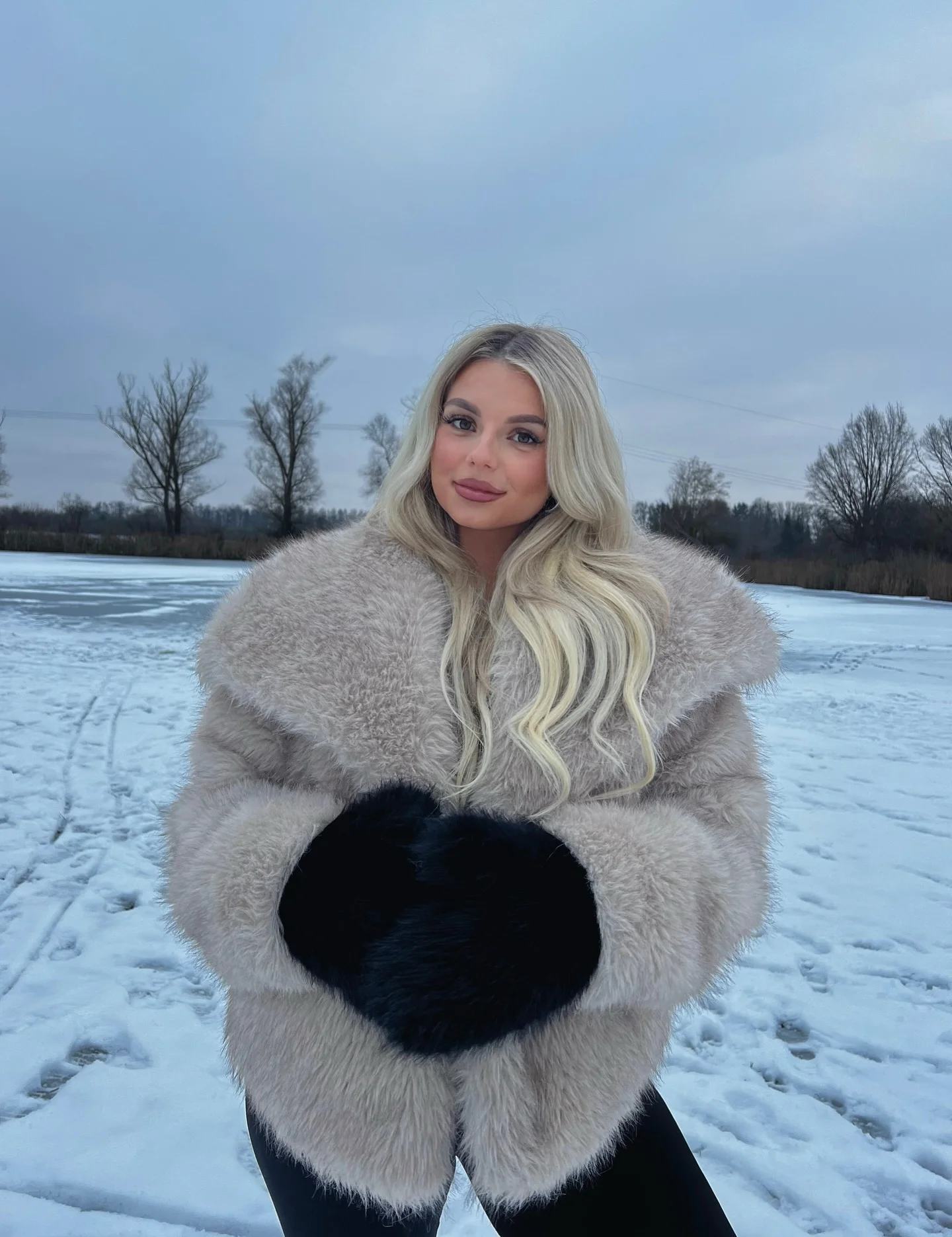 Pale gray plush-looking coat with black gloves in a snowy setting