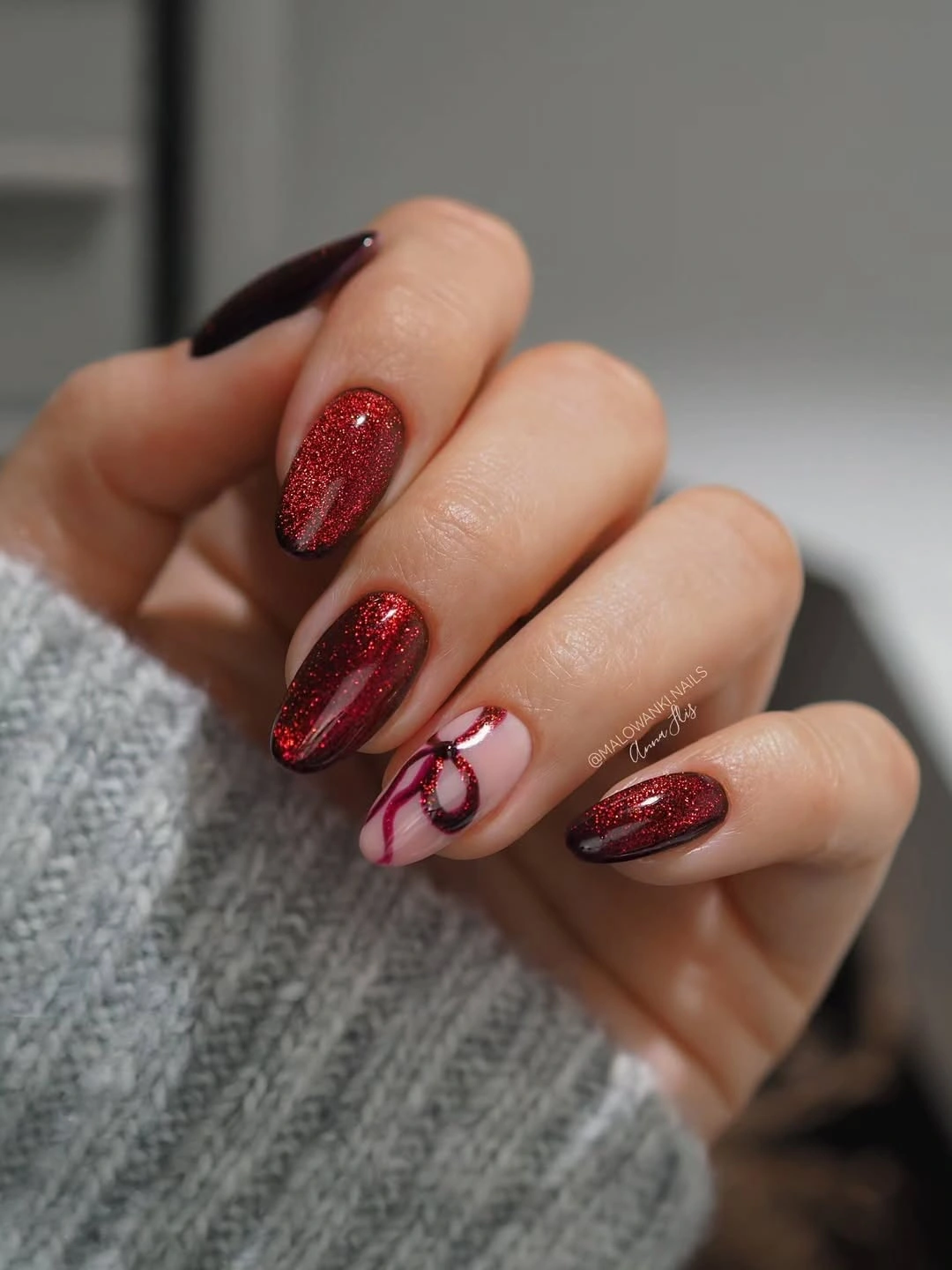 Deep red glitter almond nails with nude curved accent